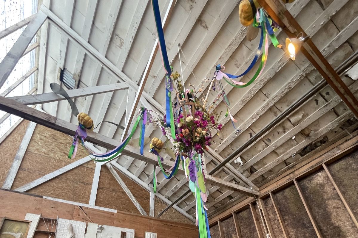 hanging from wooden rafters is a bundle of flowers, with ribbons extending outward toward other rafters